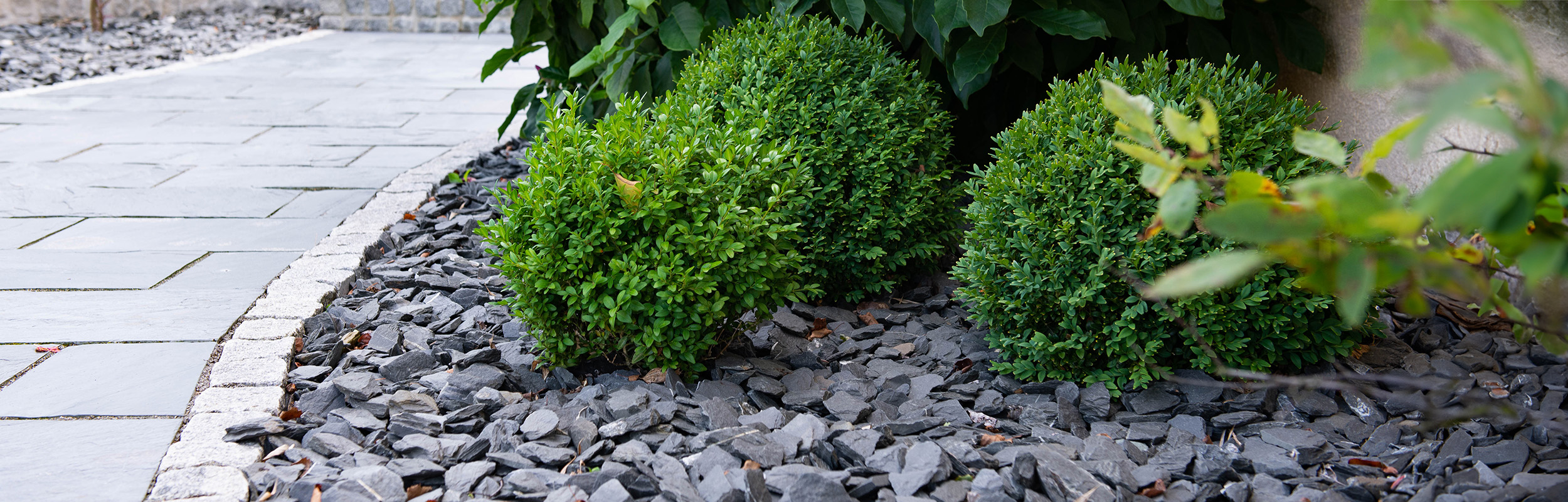 Stenrabatt med skifferkross i antracit och gatsten som kantsten mot trädgårdsgång.