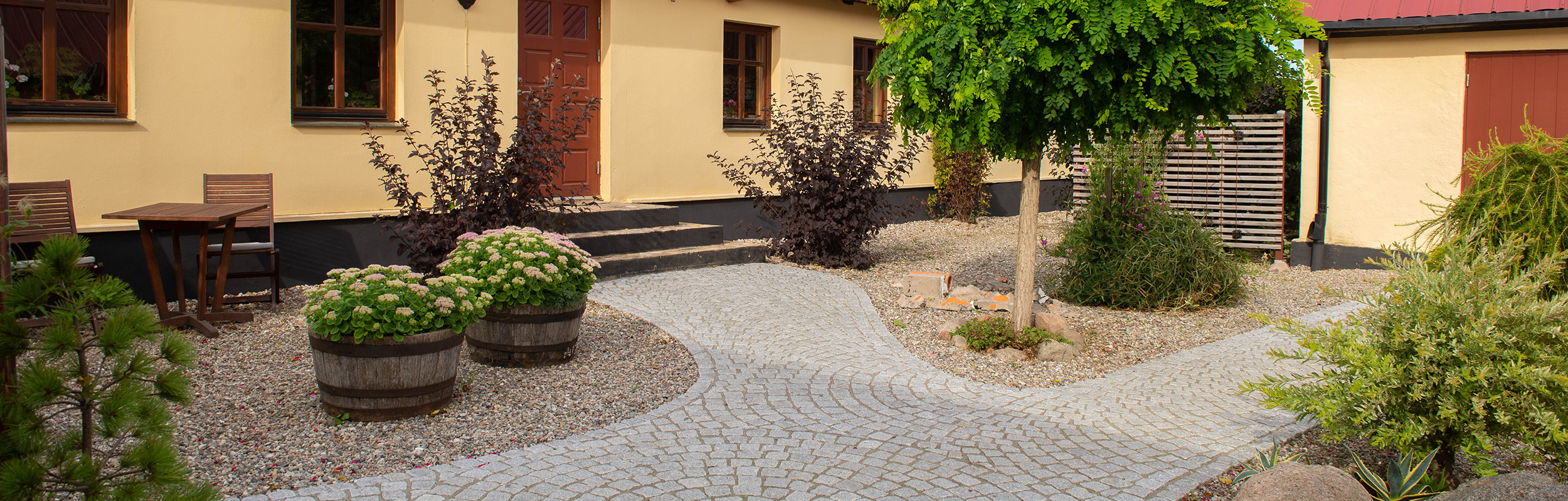 Gul sjösten i stenrabatt och gångar med gatsten famtill husentré