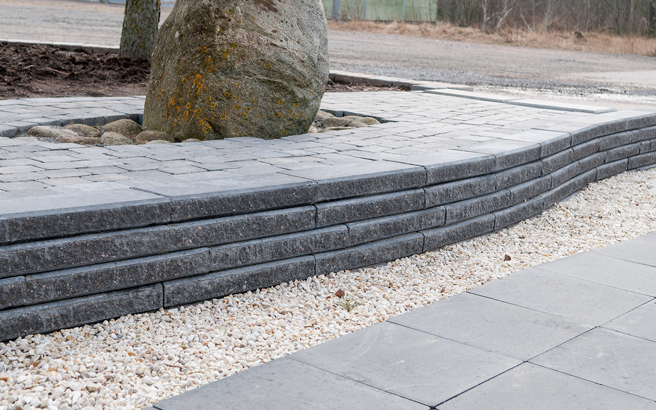 Stödmur med Knäcksten framför ett träd.